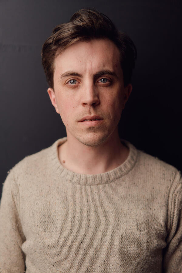 Headshot by Olivia Spencer Felix Trench wearing a rough wool jumper against a black background